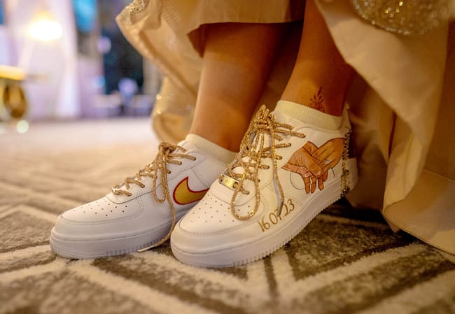Indian bride in lehenga wearing hand painted bridal Nike AF1 sneakers with bride and groom hands and choora