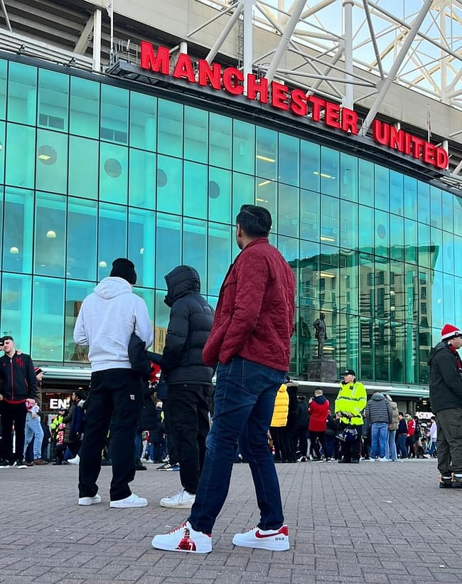 Man standing outside Manchester United football stadium wearing his custom hand painted Eric Cantona Nike AF1 sneakers - red and white