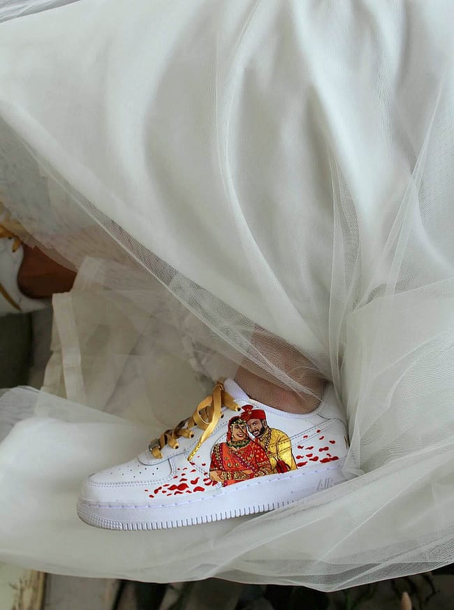 Indian bride in white dress wearing hand painted bridal Nike AF1 sneakers with bride and groom portrait on them